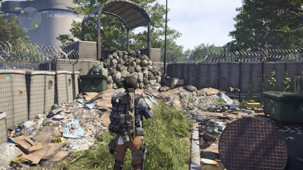 Player avatar looking at heaps of garbage near barbed wire and cement fences.