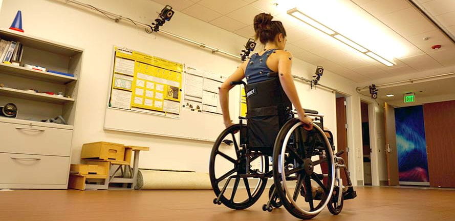 Young woman in wheelchair with reflective markers on her shoulders and arms with the Vicon Nexus Camera System overhead